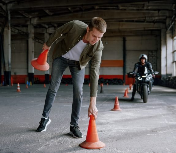 Motorbike driving school lesson with instructor putting cone on track front of student. Indoor motodrome training center